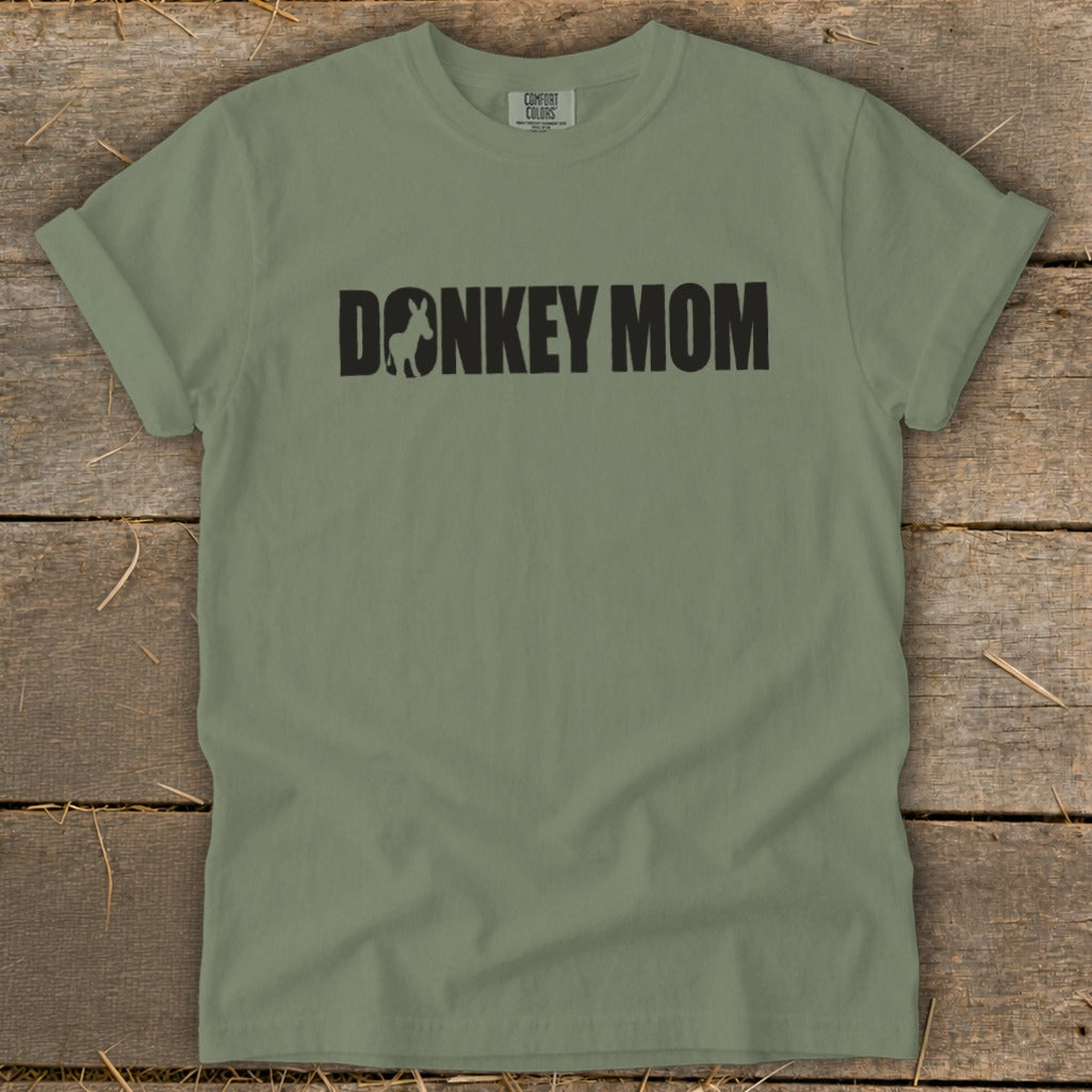 A sage green crewneck t-shirt with black text reading DONKEY MOM, featuring a donkey silhouette inside the letter O.