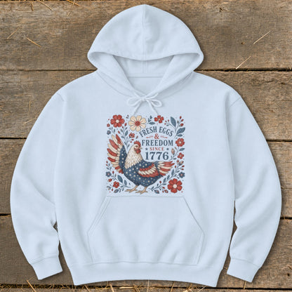 Light blue hoodie with a patriotic chicken and floral design reading "Fresh Eggs & Freedom Since 1776".