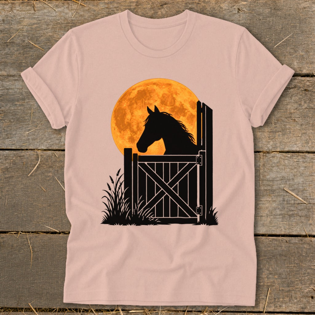 Dusty pink short-sleeved t-shirt featuring a black silhouette graphic of a horse looking over a stable gate against a large orange full moon.