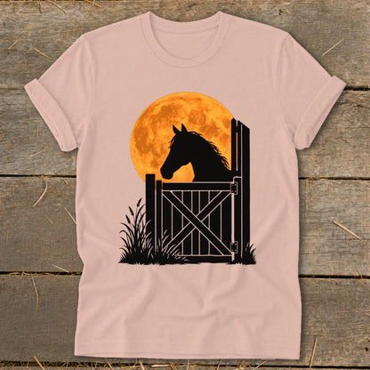 Dusty pink short-sleeved t-shirt featuring a black silhouette graphic of a horse looking over a stable gate against a large orange full moon.