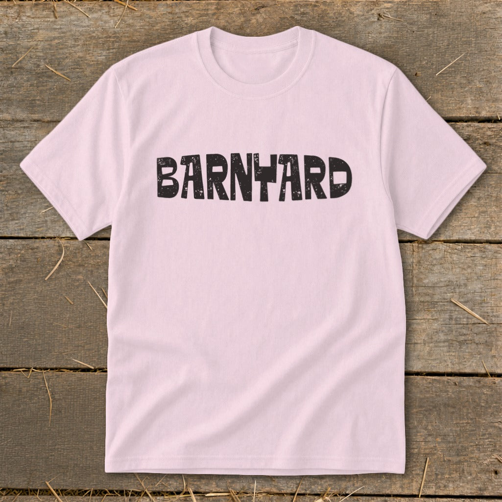 A light pink short-sleeve t-shirt with the distressed black text BARNYARD centered on the chest, laid flat on a rustic wooden background.