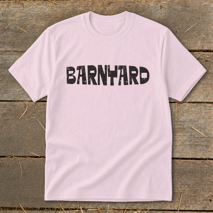 A light pink short-sleeve t-shirt with the distressed black text BARNYARD centered on the chest, laid flat on a rustic wooden background.