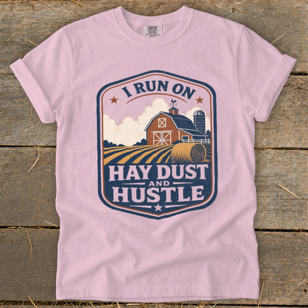 Pink t-shirt with a barn, silo, hay bale, and text reading "I RUN ON HAY DUST AND HUSTLE."
