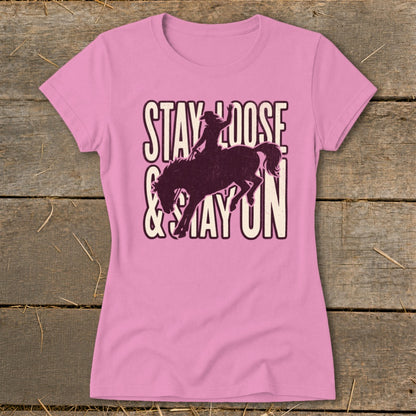 Pink t-shirt with distressed graphic of a bronco rider and text "STAY LOOSE & STAY ON".