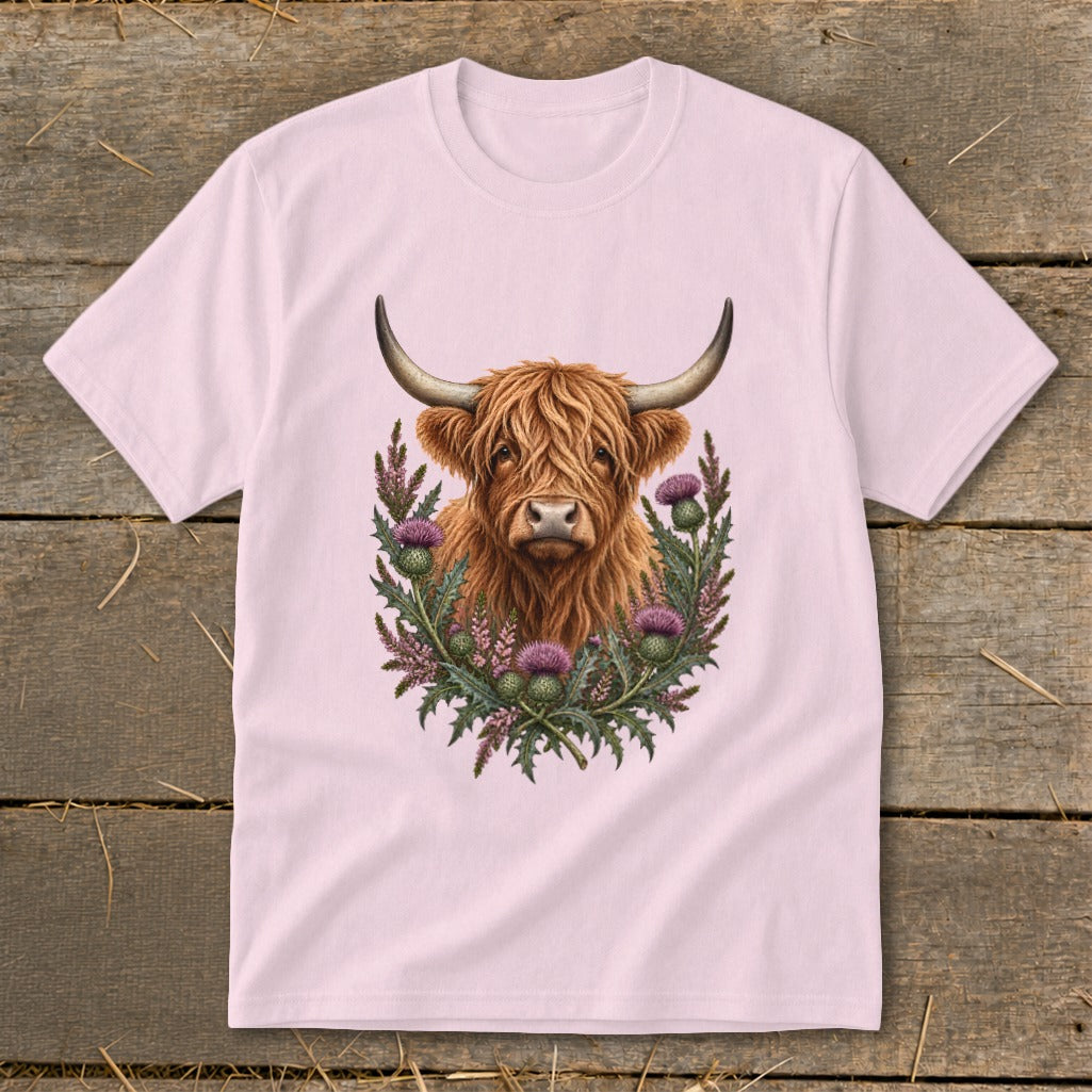 Highland cow portrait surrounded by purple thistles on a light pink t-shirt.