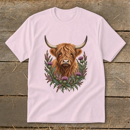 Highland cow portrait surrounded by purple thistles on a light pink t-shirt.