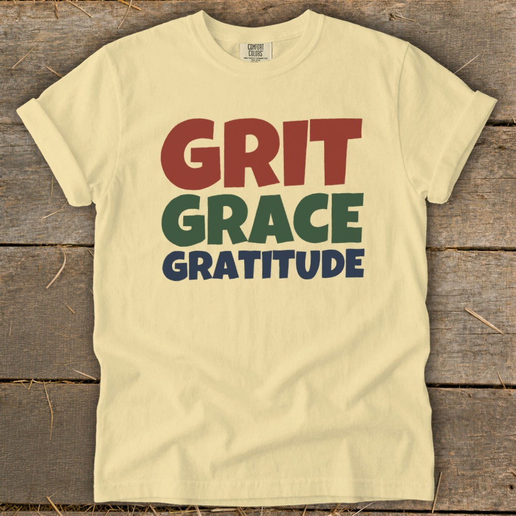 Light yellow t-shirt featuring the stacked text "GRIT," "GRACE," and "GRATITUDE" in red, green, and blue.