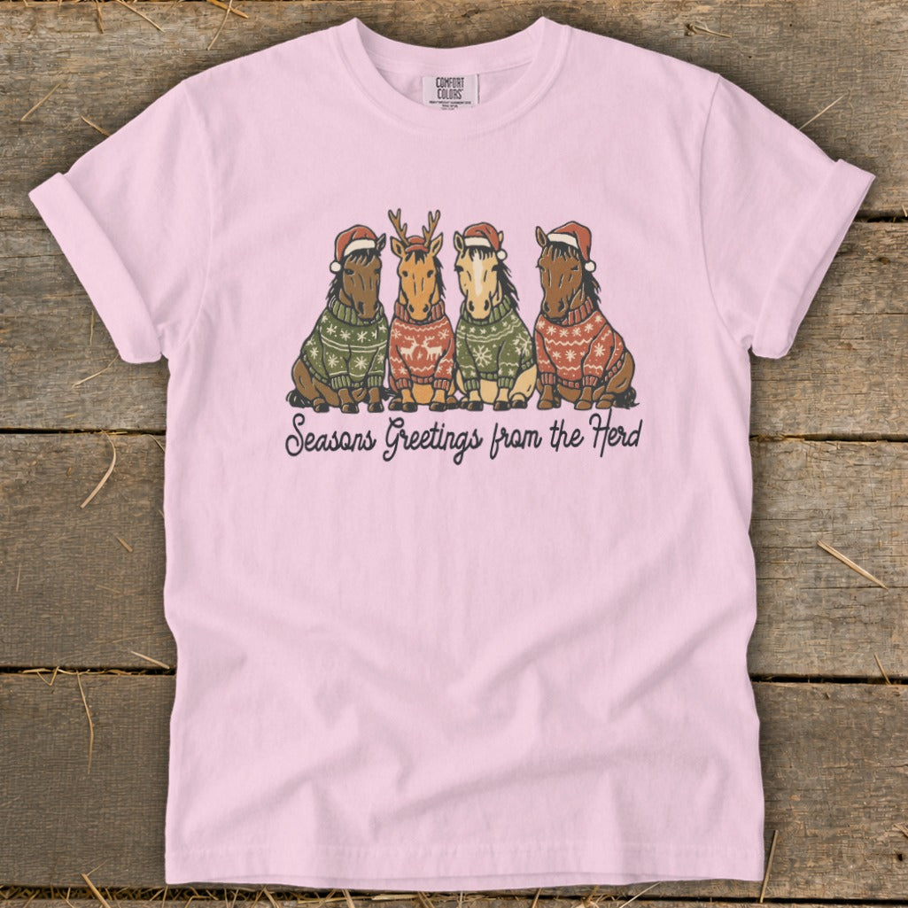 Pink t-shirt with four cartoon horses in Christmas sweaters and hats saying "Seasons Greetings from the Herd".