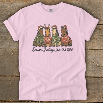Pink t-shirt with four cartoon horses in Christmas sweaters and hats saying "Seasons Greetings from the Herd".