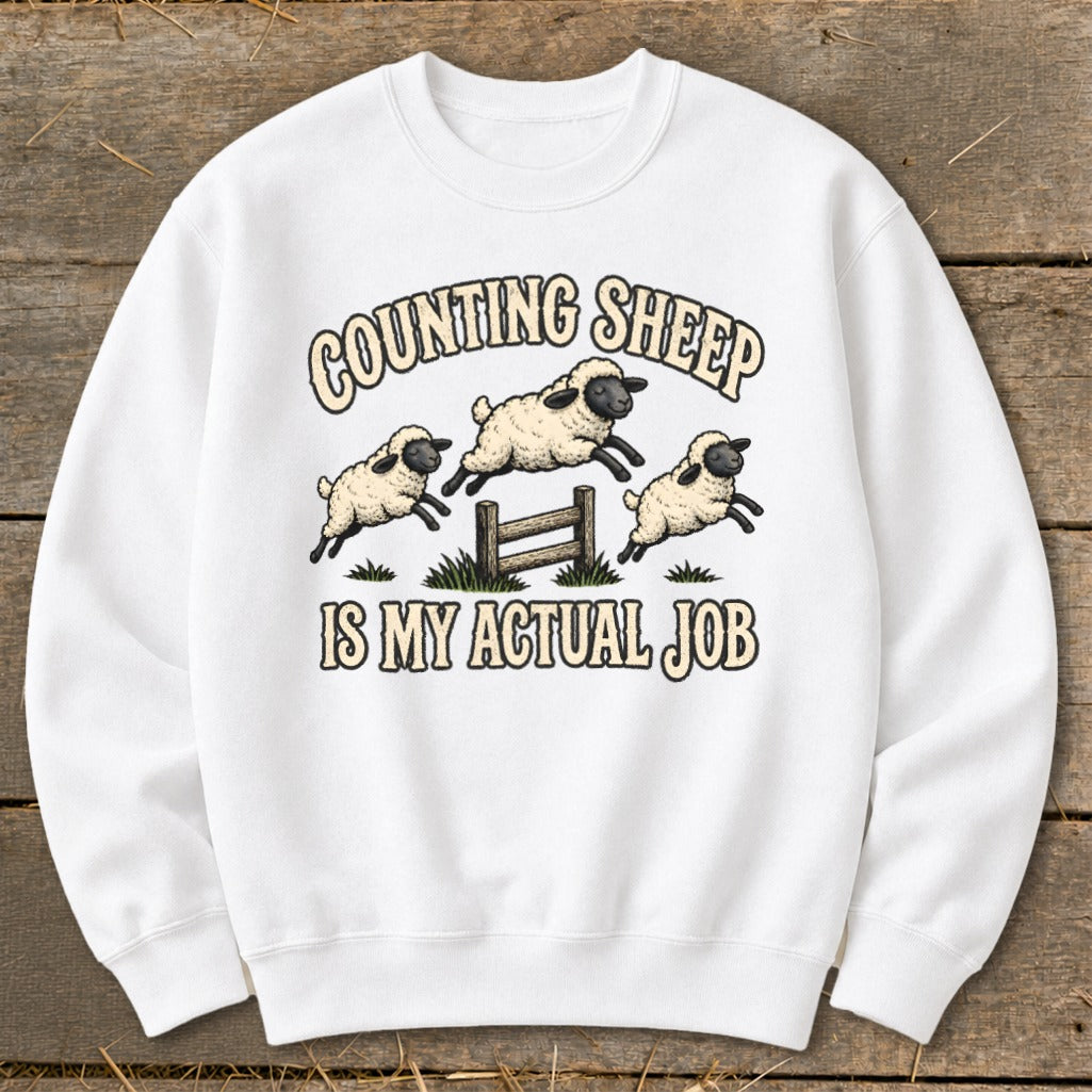 White sweatshirt with "Counting Sheep Is My Actual Job" and leaping sheep graphic.