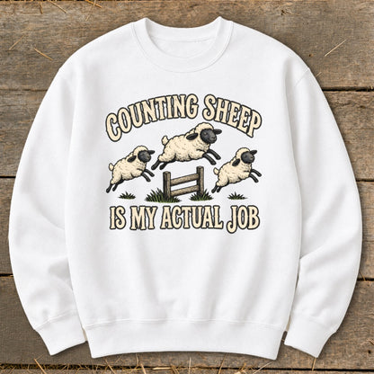 White sweatshirt with "Counting Sheep Is My Actual Job" and leaping sheep graphic.