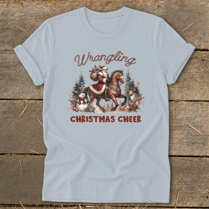 Light blue t-shirt with Santa riding a horse and the text "Wrangling Christmas Cheer."