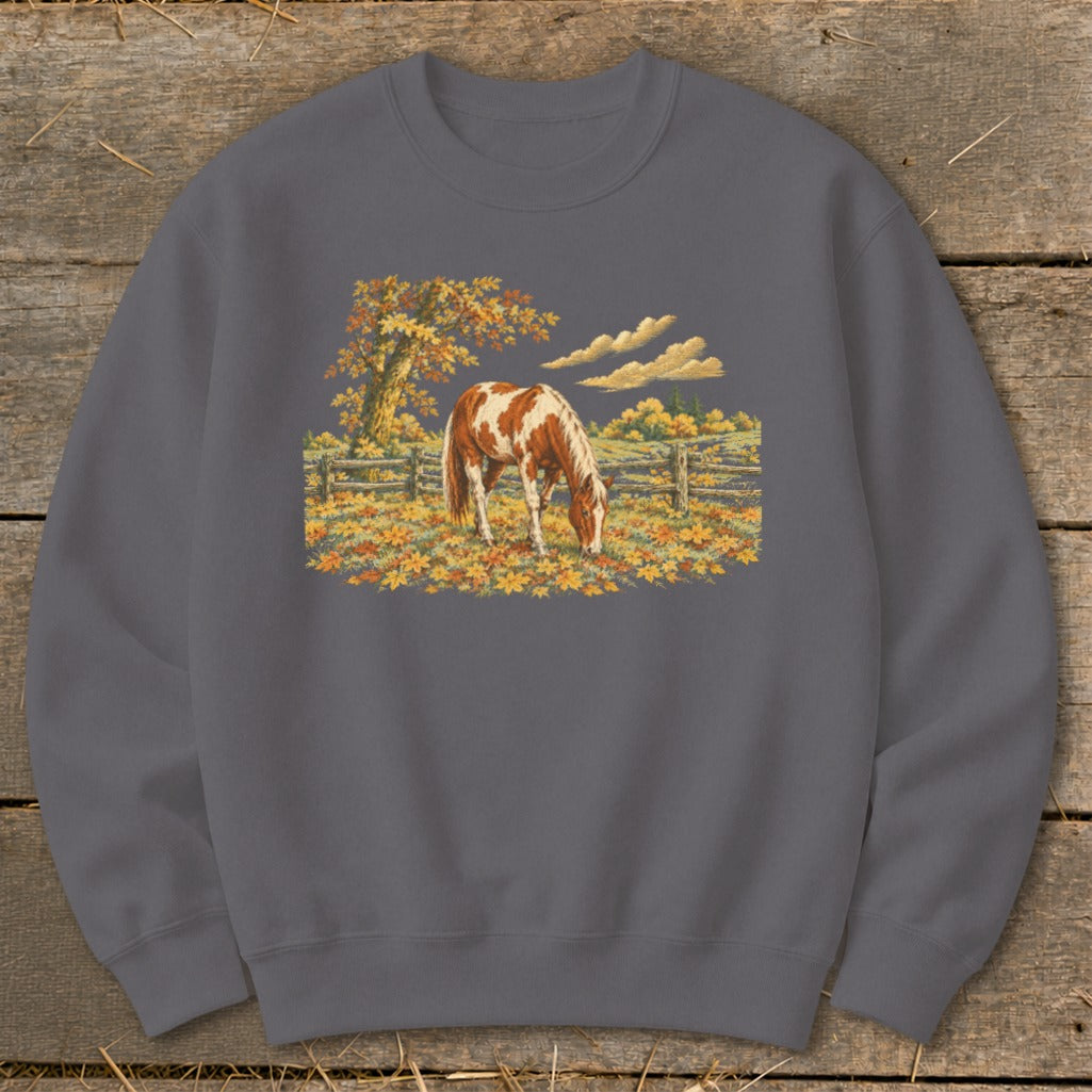 Brown and white horse grazing in a field of autumn leaves, with a tree and fence.