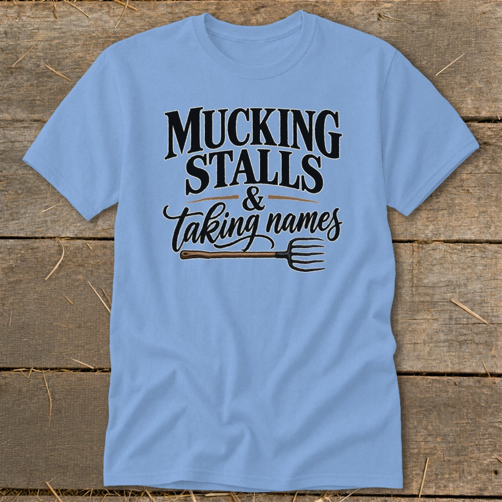 Light blue t-shirt with "Mucking Stalls & Taking Names" text and a pitchfork.