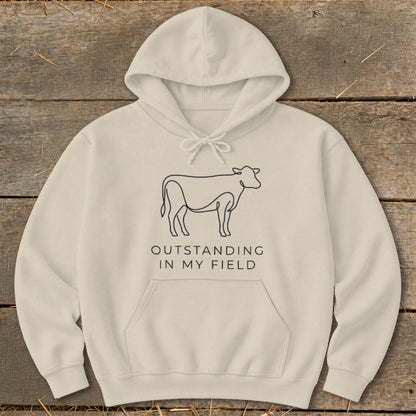 Cream hoodie with black line art cow and text "OUTSTANDING IN MY FIELD".