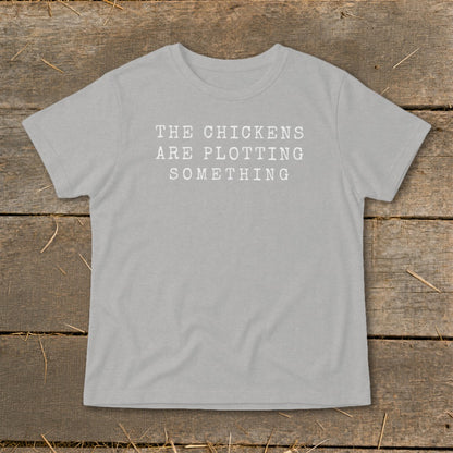 Light grey t-shirt with white text reading "The Chickens Are Plotting Something".