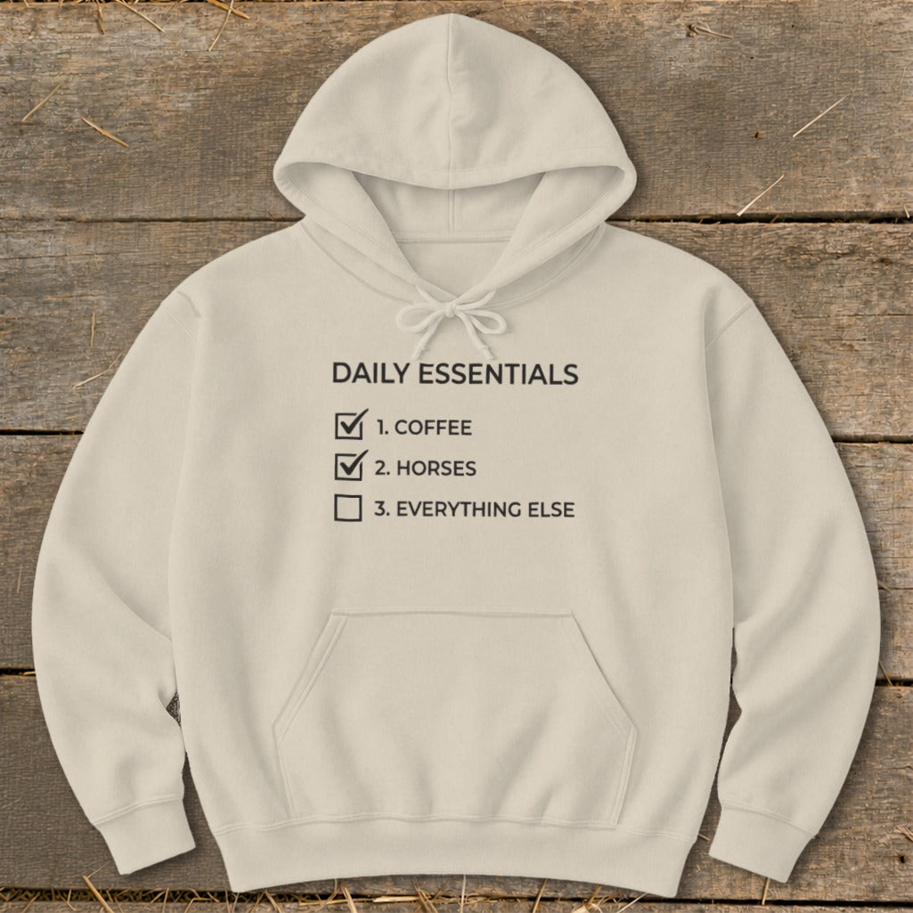 Cream hoodie with "DAILY ESSENTIALS" text listing coffee, horses, and everything else.