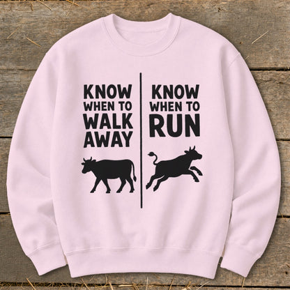 Pink crewneck sweatshirt with black text "KNOW WHEN TO WALK AWAY" and a walking cow silhouette.