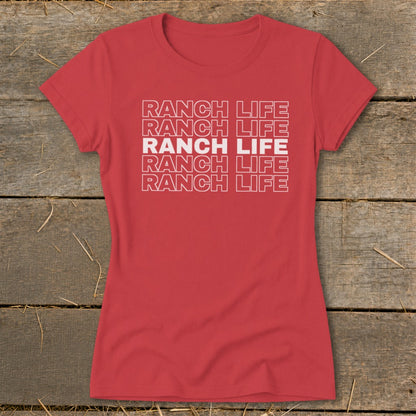 A red short-sleeved t-shirt with the text RANCH LIFE printed repeatedly on the chest lies on a wooden background.