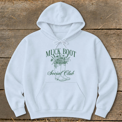 White hoodie with green "Muck Boot Social Club" text and boot graphic.