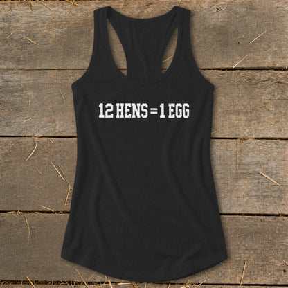 Black women's racerback tank top featuring the white text 12 HENS = 1 EGG on a wooden background.
