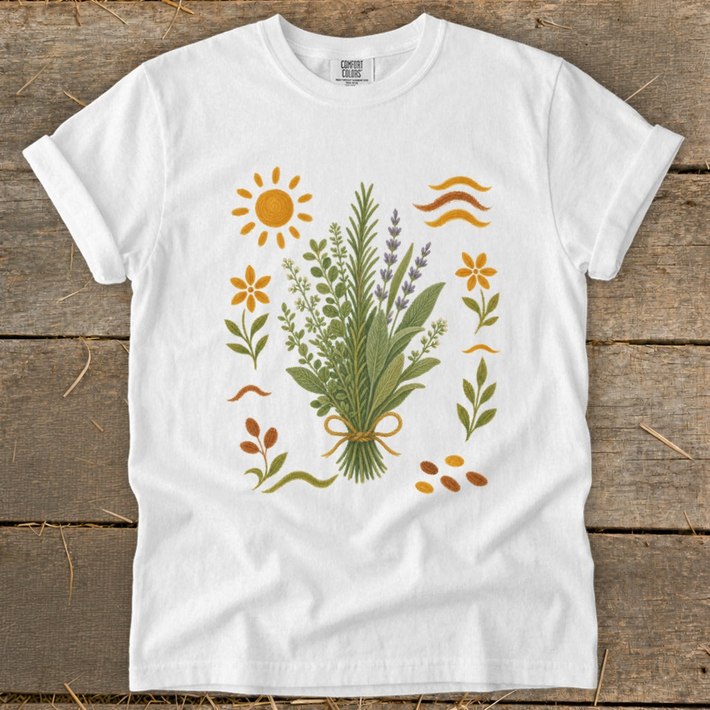 White t-shirt with botanical illustration of herbs, flowers, sun, and wavy lines.