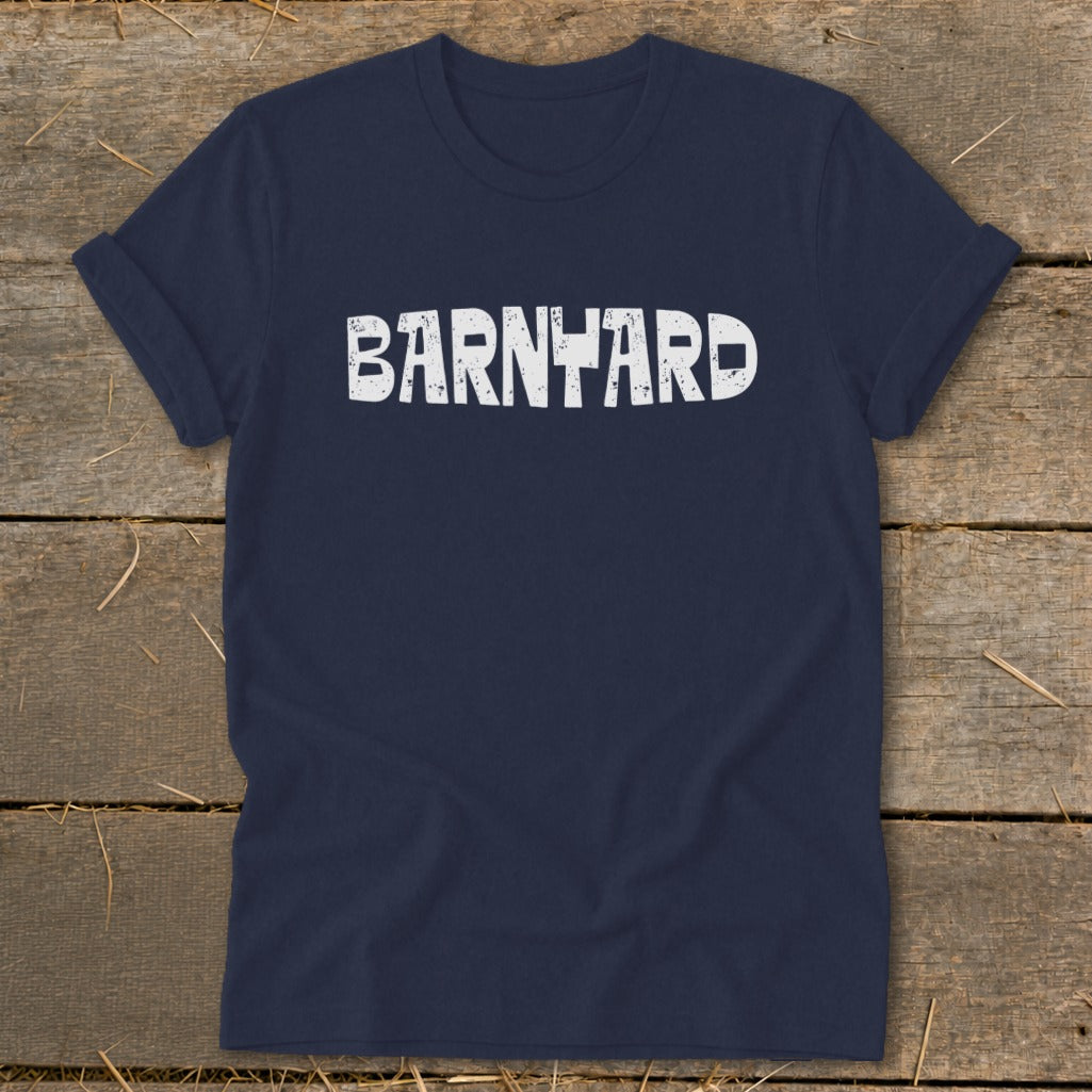 Navy blue crew neck t-shirt with distressed white text reading BARNYARD laid on a wooden surface.