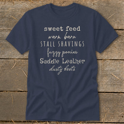 Navy t-shirt with white text: sweet feed, warm barn, stall shavings, fuzzy ponies, saddle leather, dusty boots.