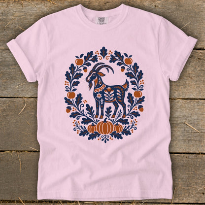 Light pink t-shirt featuring a folk-art illustration of a goat surrounded by leaves, acorns, and pumpkins.