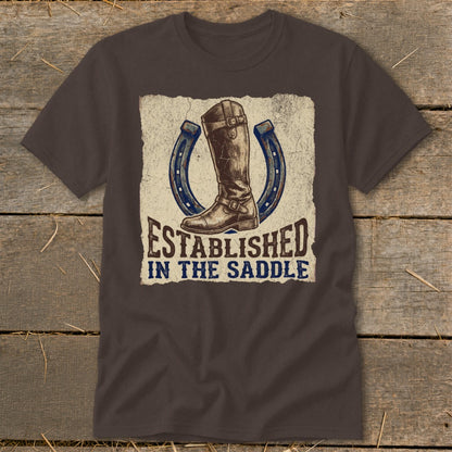 Brown t-shirt with a graphic of a boot and horseshoe, reading "Established In The Saddle".