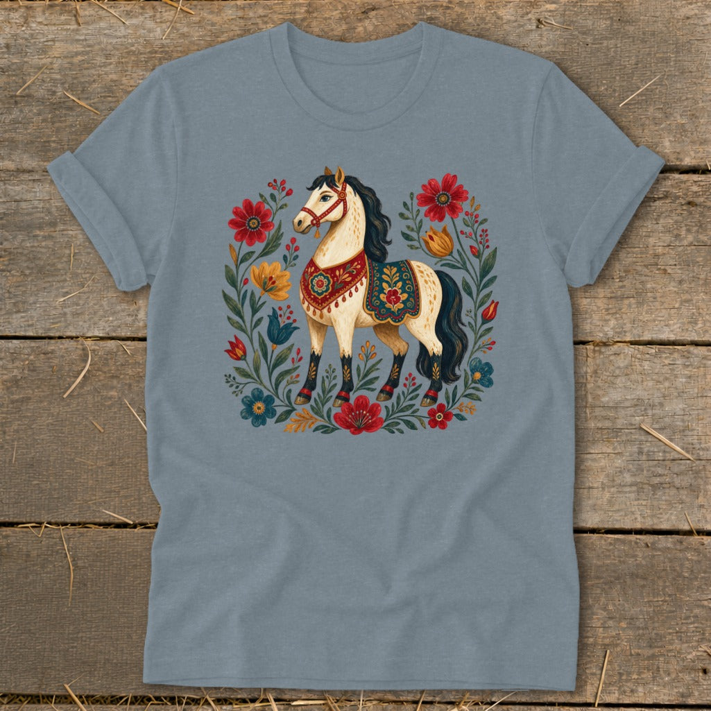Light-colored horse with decorative saddle surrounded by colorful floral motifs on a blue t-shirt.