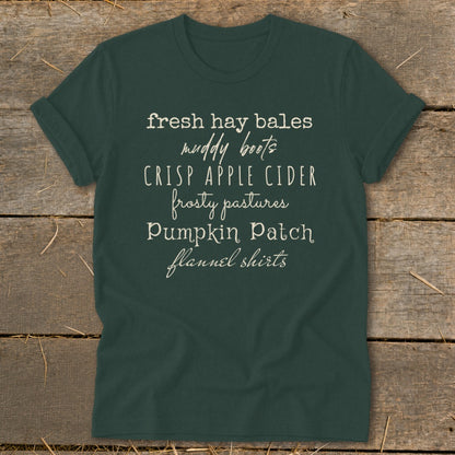 Green t-shirt with list of autumn phrases: fresh hay bales, muddy boots, crisp apple cider, frosty pastures, pumpkin patch, flannel shirts.