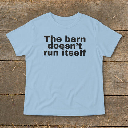 Light blue t-shirt with black text "The barn doesn't run itself" on a wooden background.
