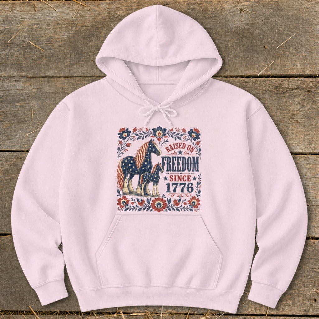 Pink hoodie with a "Raised on Freedom Since 1776" graphic featuring horses and floral elements.