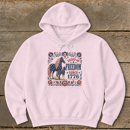 Pink hoodie with a "Raised on Freedom Since 1776" graphic featuring horses and floral elements.