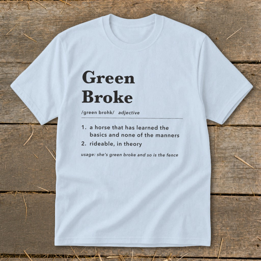Light blue t-shirt featuring dictionary-style text defining the term green broke laid flat on wood.