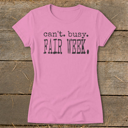 Pink t-shirt with "can't. busy. FAIR WEEK." text in dark gray.