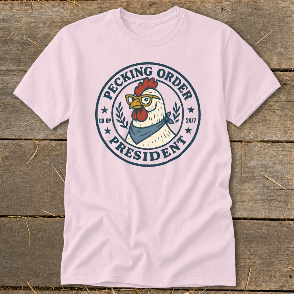 Pink t-shirt with a round logo featuring a chicken wearing glasses and a bandana, reading "Pecking Order President".