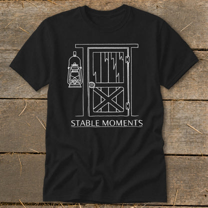 Black t-shirt with white line drawing of a barn door and hanging lantern, text "STABLE MOMENTS".