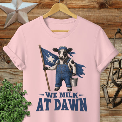Cow wearing overalls and cape, holding milk pail and flag with "We Milk at Dawn" text.