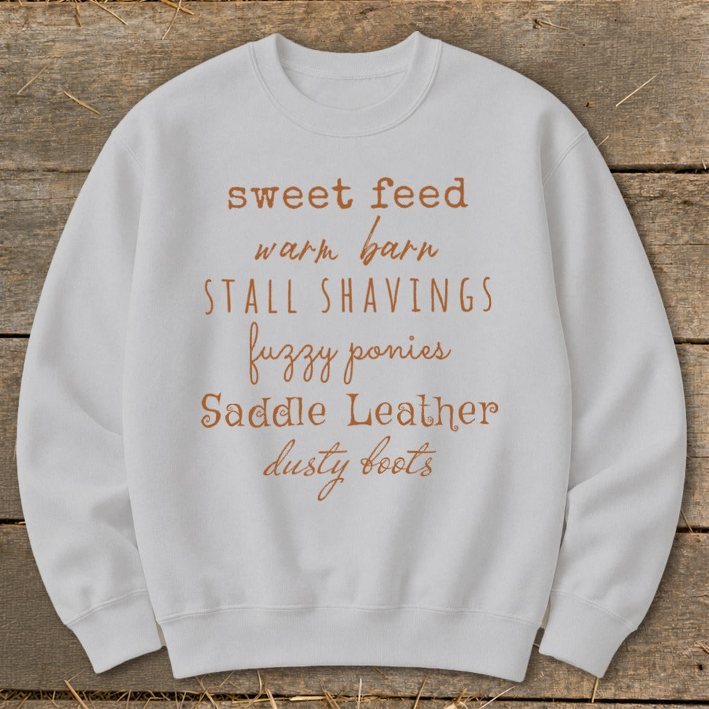 White sweatshirt with rustic font listing "sweet feed," "warm barn," "stall shavings," "fuzzy ponies," "saddle leather," "dusty boots."