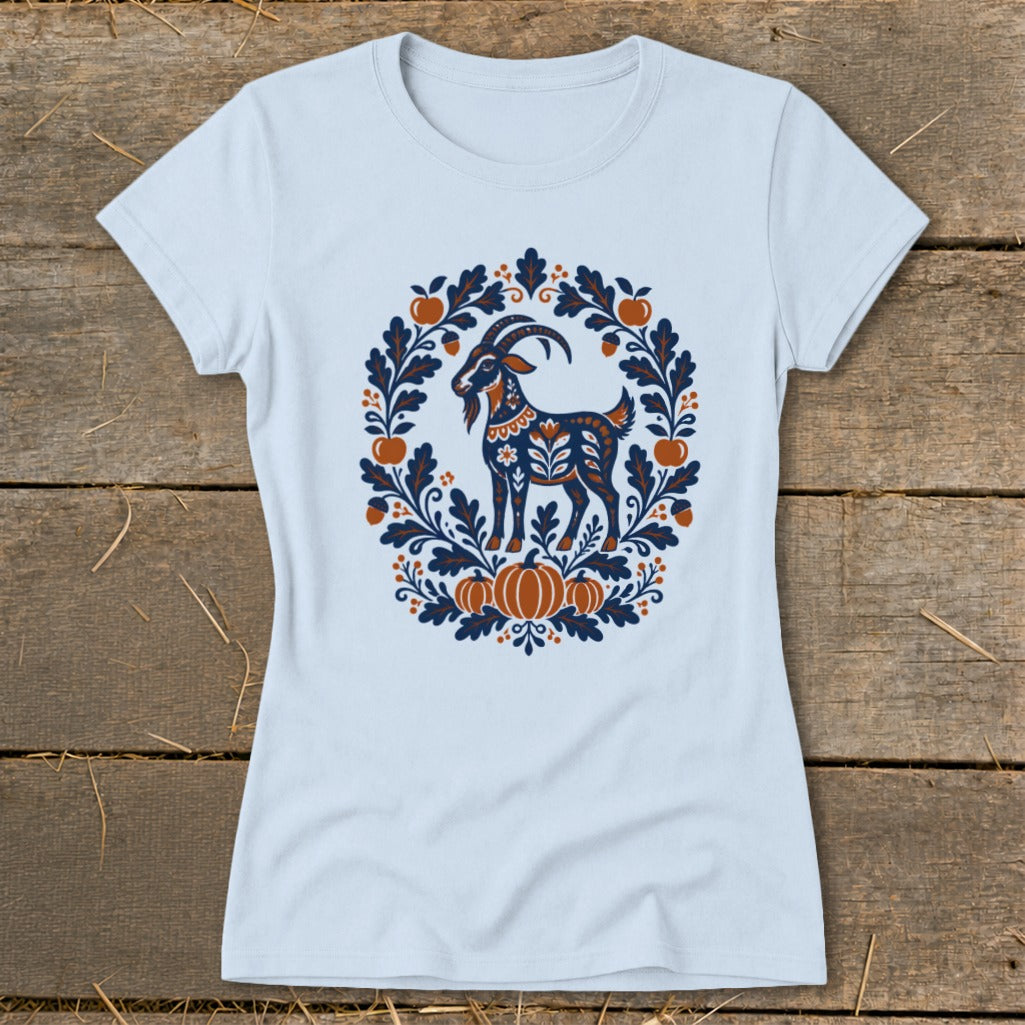 Light blue women's t-shirt featuring a folk art graphic of a goat framed by autumn leaves and pumpkins.