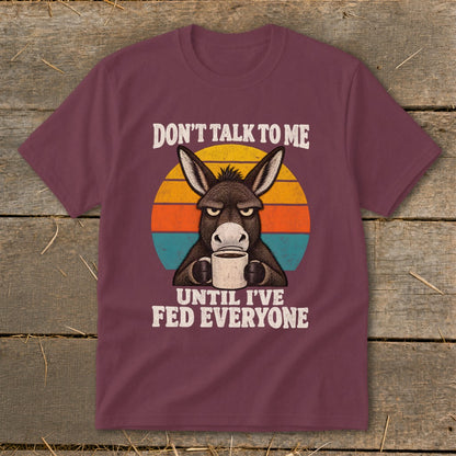 Maroon t-shirt featuring a grumpy donkey holding a mug against a striped sunset graphic with text.
