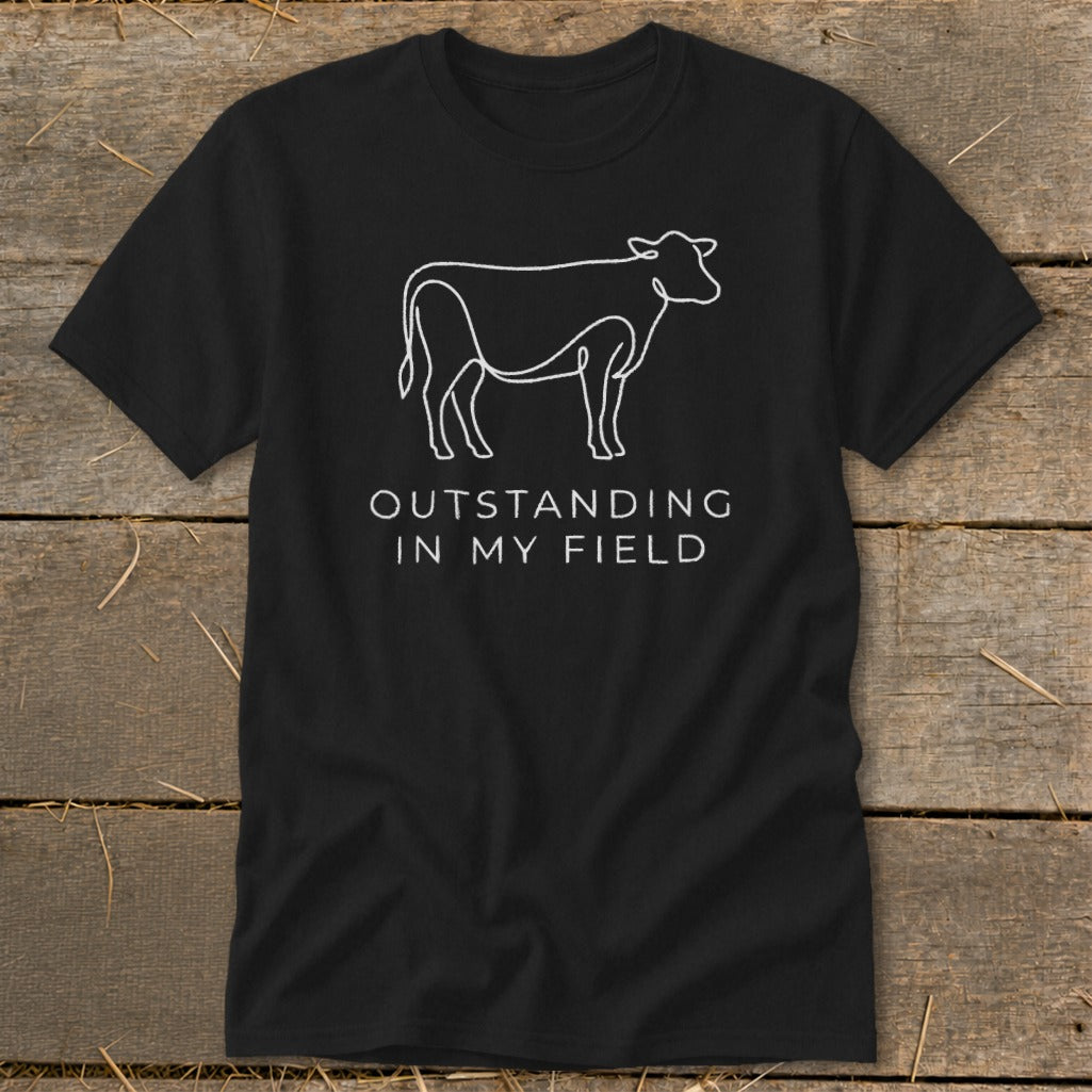 Black t-shirt with a white line drawing of a cow and the text "OUTSTANDING IN MY FIELD".