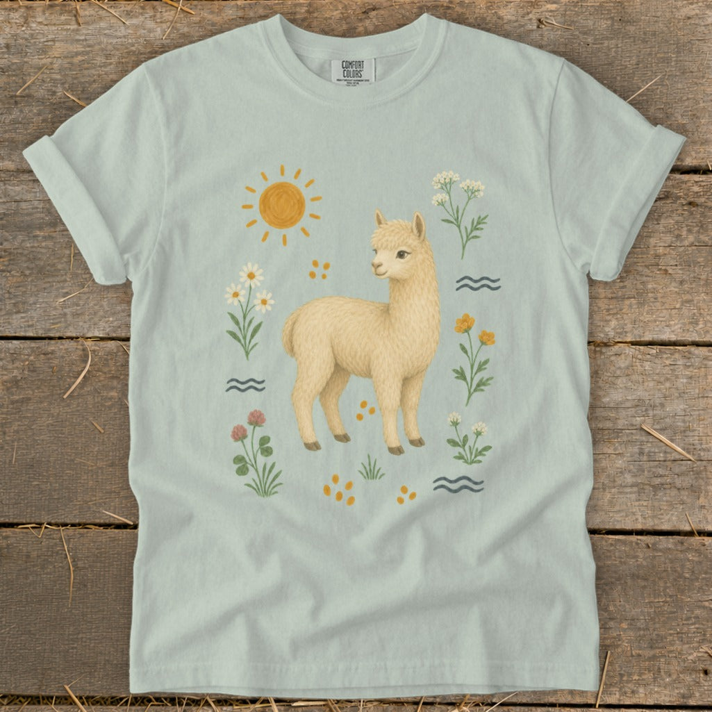 Light blue t-shirt with a cream alpaca surrounded by flowers and sun graphic.