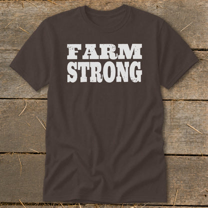 Dark brown crewneck t-shirt featuring the distressed white text FARM STRONG across the chest, laid flat on a rustic wooden background.