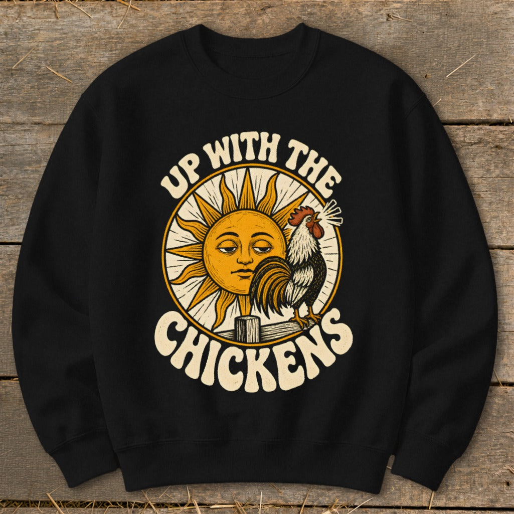 A black crewneck sweatshirt printed with a vintage illustration of a sun and rooster, captioned Up With The Chickens.