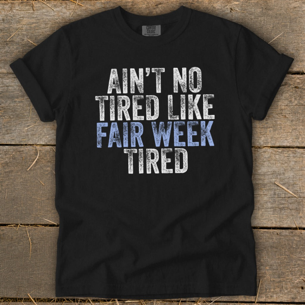 Black t-shirt with white and blue distressed text saying "Ain't No Tired Like Fair Week Tired".