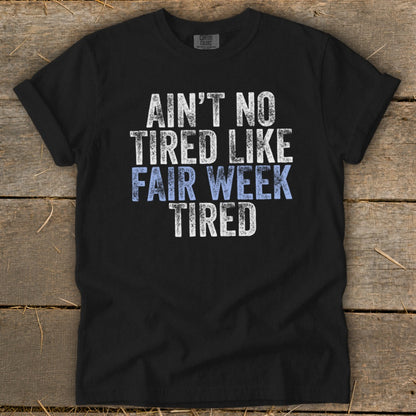 Black t-shirt with white and blue distressed text saying "Ain't No Tired Like Fair Week Tired".