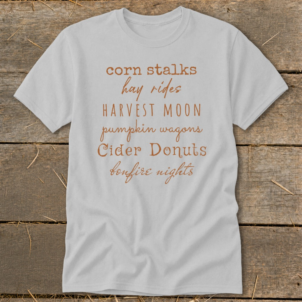 Light gray t-shirt with fall phrases: corn stalks, hay rides, harvest moon, pumpkin wagons, cider donuts, bonfire nights.